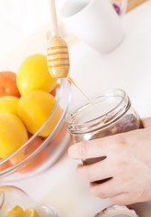 Close up of hands with honey dipper in the air and citrus fruits served on wooden tray
