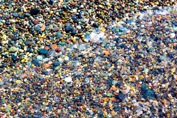Small colorful wet stones and water on beach in seacoast
