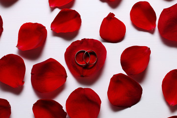Gold wedding rings on a petal of a red rose on a white wooden table.