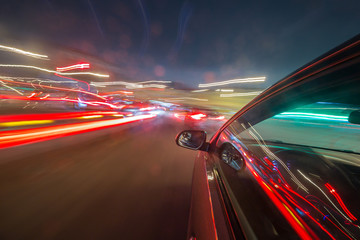 Obraz premium View from Side of Car moving in a night city, Blured road with lights with car on high speed. Concept rapid rhythm of a modern city.