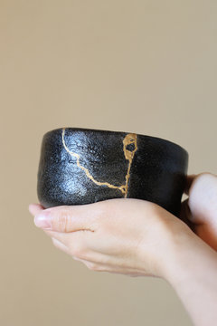 女性が両手で持つ金継ぎ黒楽茶碗 茶道の所作 ぼかし背景 縦位置