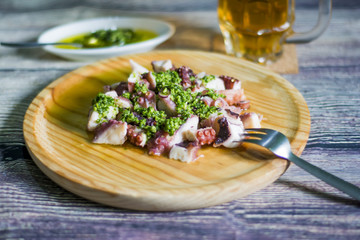Octopus with paprika, a pitcher of beer and sauce on a wooden ta
