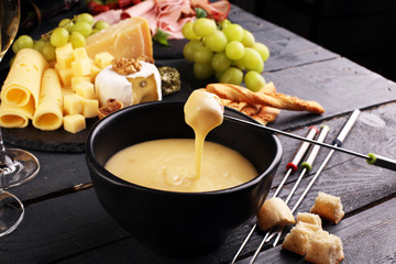 Gourmet Swiss fondue dinner on a winter evening with assorted cheeses on a board alongside a heated pot of cheese fondue with two forks dipping bread and white wine behind in a tavern or restaurant
