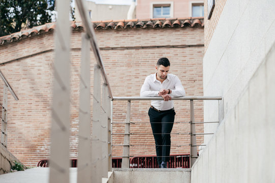 Businessman Checking The Time On Wristwatch While Leaning On Rai