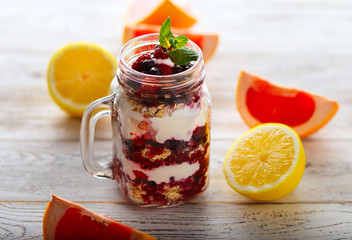 Muesli, fresh berries and yogurt in glass mason jar on wooden table.