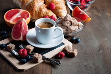 Coffee and croissants with raspberries and fruits for breakfast. Toned image, selective focus, copy space
