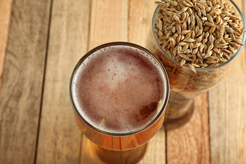 Glasses with fresh beer and barley on wooden background