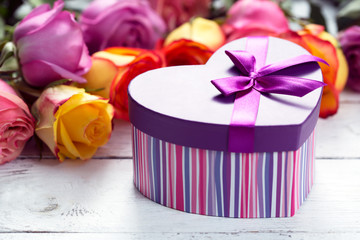 Box present on the forefront, purple and yellow roses at the wooden table