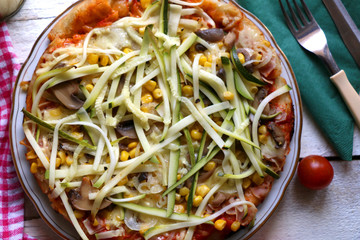 Homemade vegetarian pizza with lot of toppings: tomato sauce, mozzarella, zucchini, corn and champignons. Top view.
