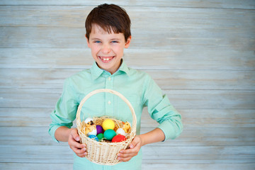 Cute little boy holding basket with colorful eggs after easter egg hunt