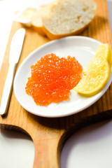 Red caviar, lemon and bread on wooden board white table background