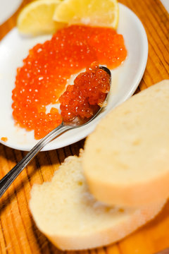 Red caviar, lemon and bread on wooden board white table background