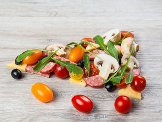 Creative composition of ingredients tomatoes, cheese, salami, mushrooms, arugula, olives in the form of a slice of pizza