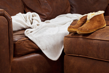 Slippers and throw blanket on a soft brown leather sofa