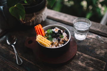 Close up of the bowl of smoothie with exotic fruits (papaya, mango, pineapple, blueberry) and nuts on the wooden table. Great vegetarian and helthy breakfast in Indonesia, Bali