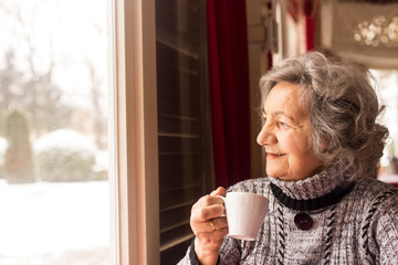 Senior woman drinking coffee and looking through window