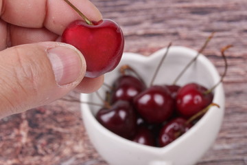 Hand-picked cherriy and cherries in heart-shaped mug on wooden.