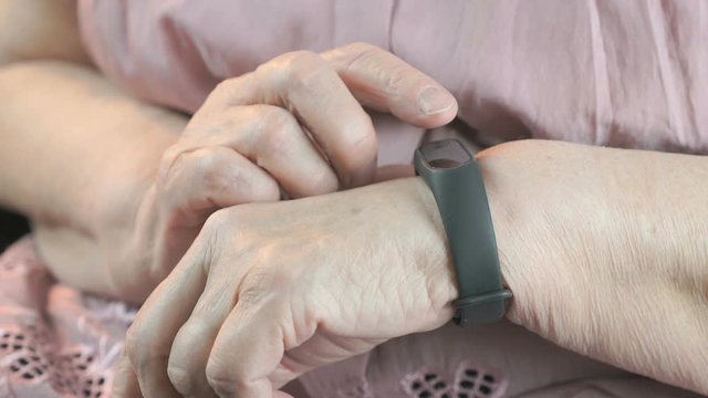 Black smartband. The elderly woman looks at the results of physical activity using the smart fitness tracker