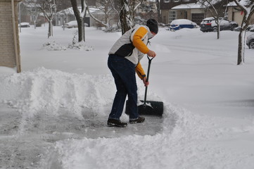 Winter scene - a tall Caucasian man shovels a driveway in a residential area in Ontario Canada
