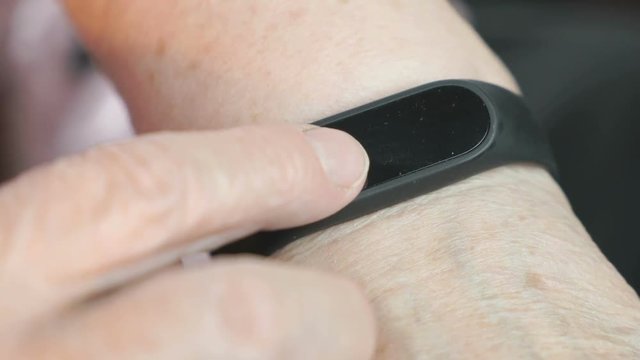Black smartband. The elderly woman looks at the results of physical activity using the smart fitness tracker