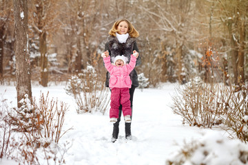 Fototapeta na wymiar Mother raises hands daughter outdoors. Family walk in a winter park. Family happiness.