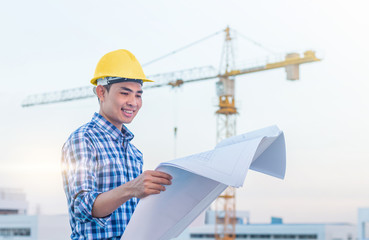 The man worker wear a yellow helmet and hold the blueprint with