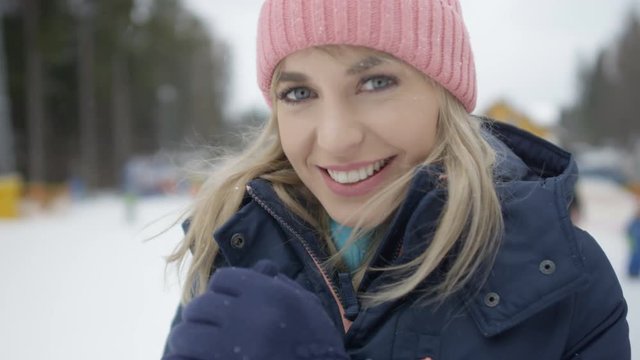 Portrait of a young smiling woman in winter clothing waiting for her friends near ski lift. 