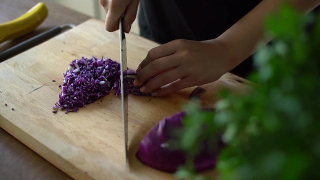 Woman chopping fresh red cabbage on a wooden table in kitchen