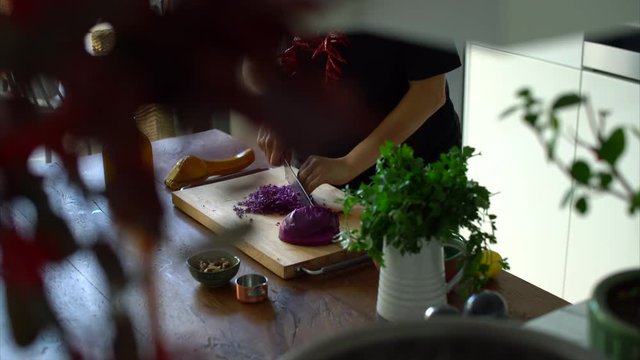 Woman chopping fresh red cabbage on a wooden table in kitchen