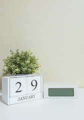 White wooden calendar with black 29 january word with clock and plant on white wood desk and cream wallpaper textured background , selective focus at the calendar