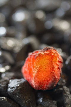 Red hot coal nugget on focus on other cold raw nuggets of coal. Background of raw coals with soft focus exclusion with color and temperature.