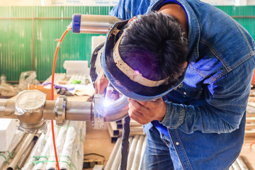 Industrial worker with protective mask welding metal piping using tig welder