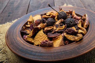 Dried fruit (apples, pears, apricots), berries in a bowl on dark wooden background. Close up. Ingredients for the winter vitamin drink, compote.