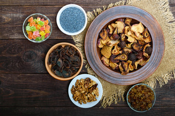 Dried fruit (apples, pears, apricot), berries, walnut kernels, raisins, poppy seeds in a bowl on dark wooden background. The top view. The ingredients for the porridge.