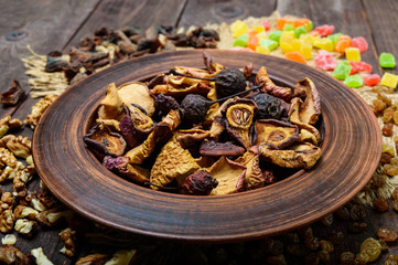 Dried fruit (apples, pears, apricots), berries, raisins and nuts in a bowl on dark wooden background. Close up. Ingredients for the winter vitamin drink, compote.