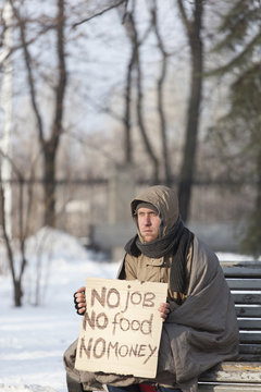  Young  depressed  homeless man with cardboard  in  winter city park