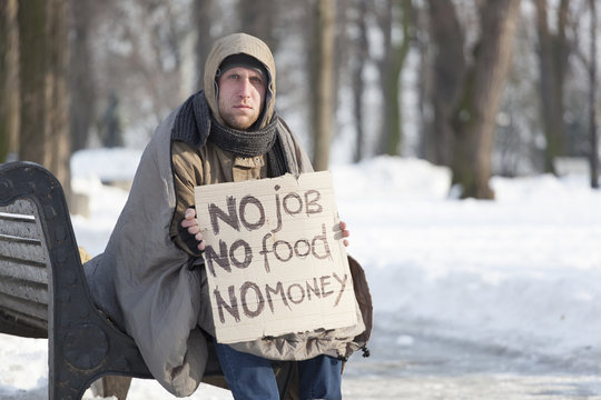 
 Young   Hungry  Homeless Man In  Winter City Park Ask Help By Cardboard
