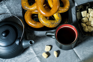 Bagels, coffee cup, teapot and sugar in black on a blue tablecloth. View from above