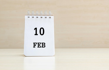 Closeup surface note book with black 10 feb word in page on blurred brown wood desk and wood wall textured background with copy space under window light