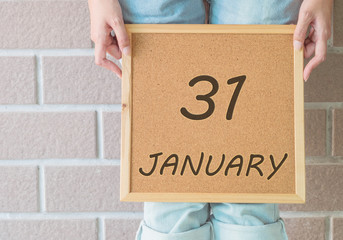Closeup calendar at the cork board in hand of asian woman in front of her legs with 31 january word on brick wall textured background