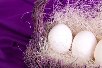 Easter. White eggs in purple basket on violet background. Copy space. Top view.