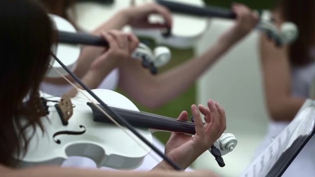 Girl in white dress plays on white violin. Violin close-up.

