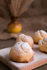 Profiteroles with powdered sugar on wooden background. Rustic style. Close up.