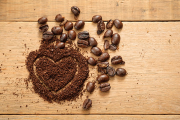 ground coffee in heart shape close to coffee beans on wooden table