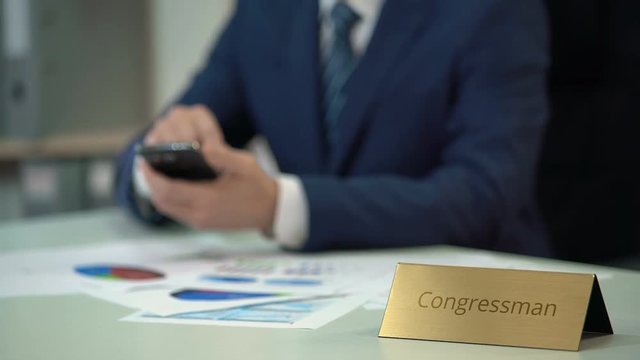 Serious congressman using smartphone, working on diagrams for election program