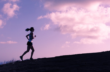 Silhouette of female runner running up a hill.