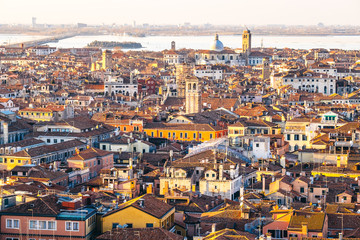 Naklejka premium Aerial view of Venice, Italy, at sunset with rooftops of buildings and warm sunlight.