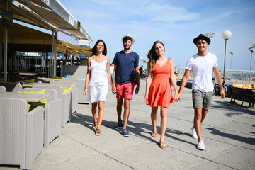 Group of young people man and woman walking on seaside of touristic resort during a sunny summer day