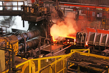 Hot steel bar being rolled to desired shape in modern industrial mill at high temperature. © Paul