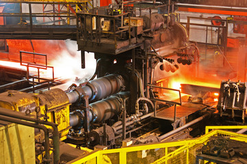 Hot steel bar being rolled to desired shape in modern industrial mill at high temperature.